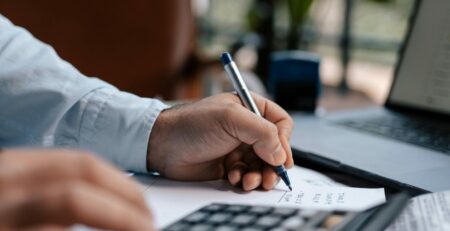 Free A person calculating finances with a calculator and pen on a desk indoors. Stock Photo