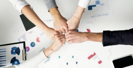 Free Colleagues celebrate success with a fist bump over financial charts depicting teamwork and unity. Stock Photo