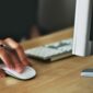 Free A hand using a wireless mouse at a modern desk setup with a computer and keyboard. Stock Photo